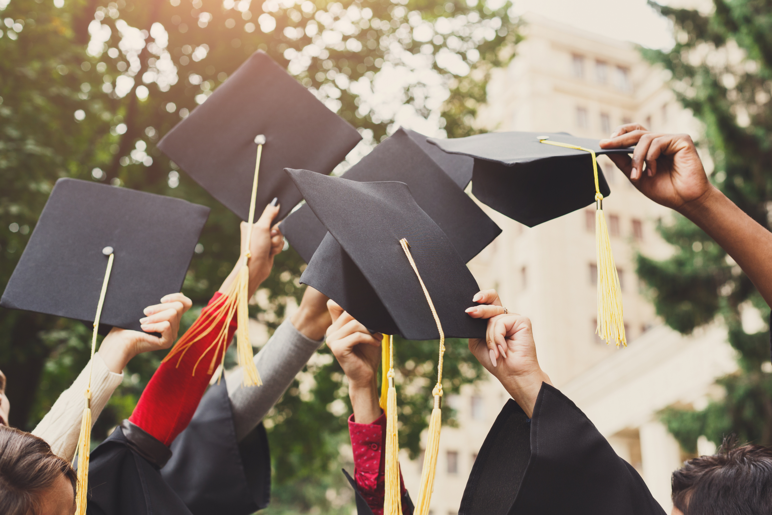 Graduating students hold their mortarboards in the air